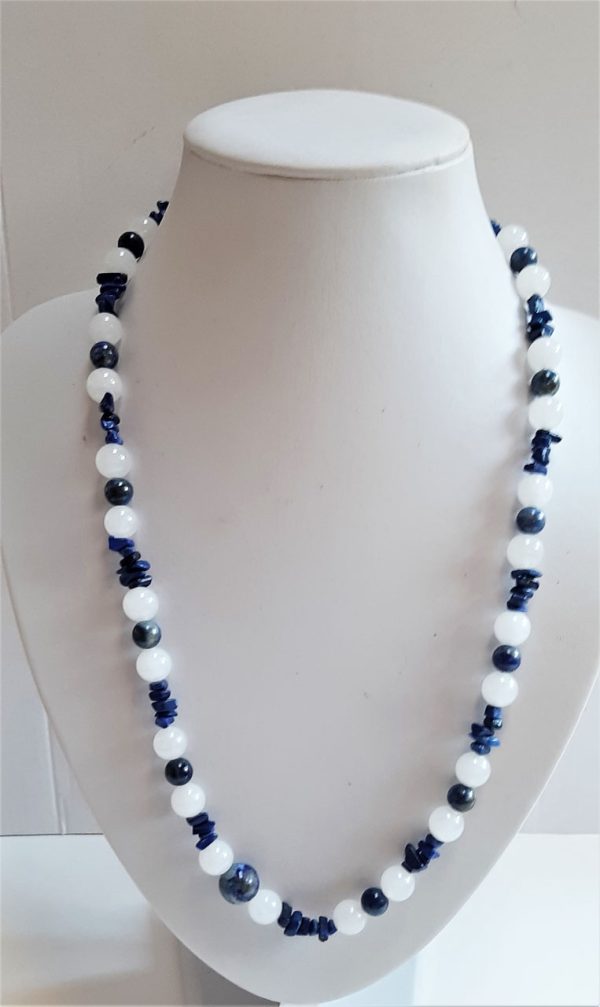 Auf dem Bild ist eine Edelsteinkette aus Lapislazuli und Jade auf einer weißen Büste zu sehen. Die Steine sind aus dunklem Blau und weiß. Die Kette ist relativ lang.