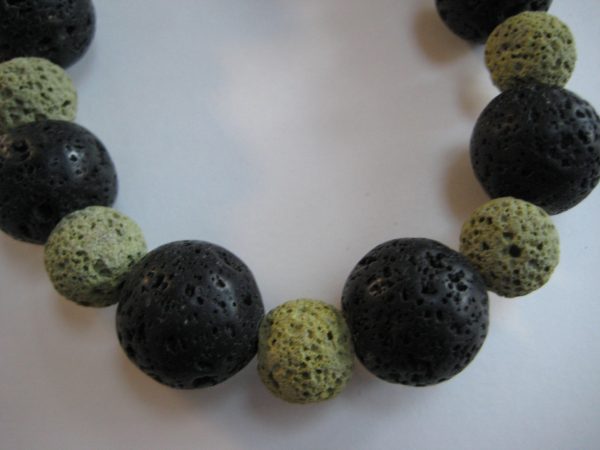 Zoom auf einzelne kleine grüne und größere schwarze Lavasteinperlen einer Edelsteinkette aus Lavastein.