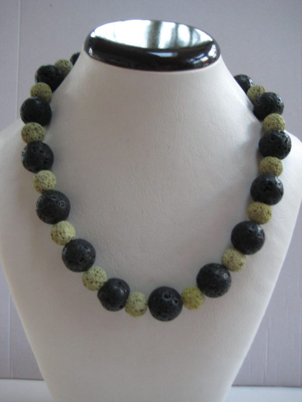 Eine Edelsteinkette aus Lavastein mit grünen und schwarzen Steinen auf einer weissen Damenbüste aus Kunststoff.