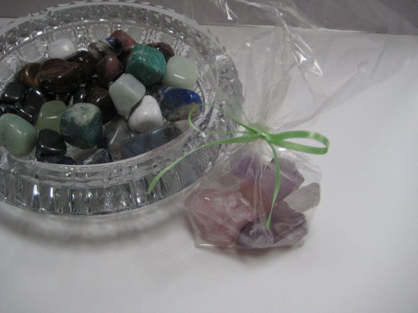 Rosenquarz-Amethyst-Bergkristall: Die einzelnen Edelsteine des Produkts Wasserbelebung mit Edelsteinen - Grundmischung in einem Säckchen, Daneben eine Glasschale mit weiteren Edelsteinen.