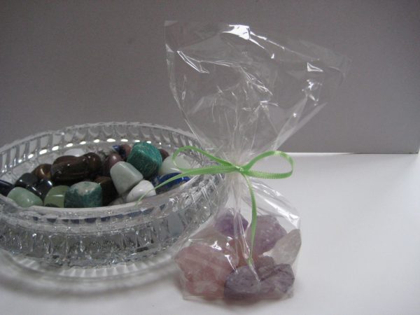 Rosenquarz-Amethyst-Bergkristall: Die einzelnen Edelsteine des Produkts Wasserbelebung mit Edelsteinen - Grundmischung in einem Säckchen, Daneben eine Glasschale mit weiteren Edelsteinen.