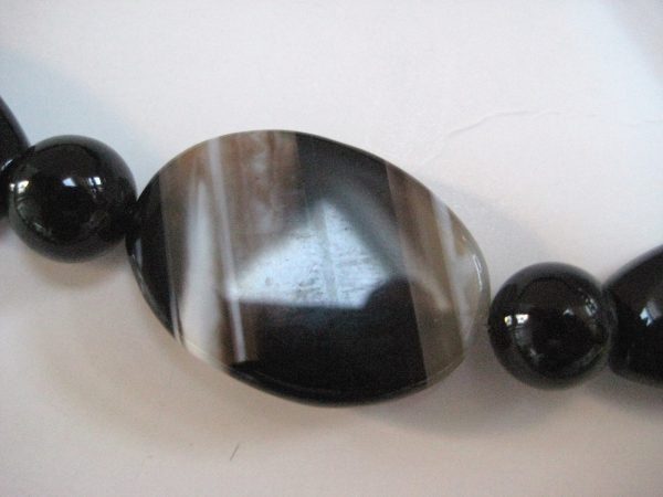 Zoom auf einen ellipsenförmigen Achatstein einer Edelsteinkette aus Achat und Onyx mit Steinen in Grau- und Schwarztönen.