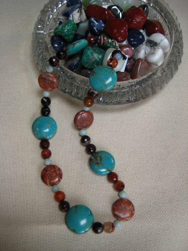 Farbenprächtige Edelsteinkette aus Achat, Tuerkis, und Amazonit aus einer Glasschale fließend.