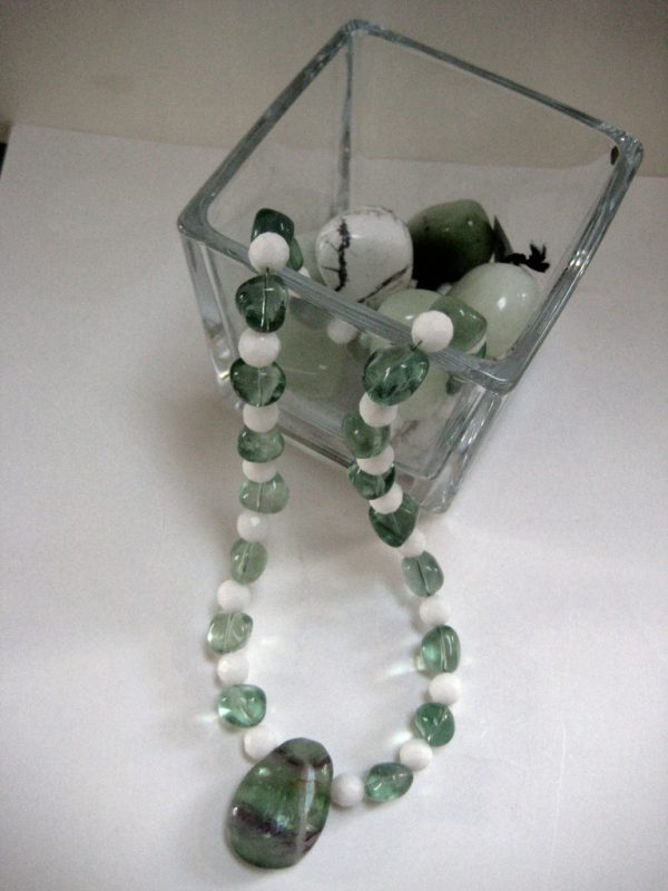 Aufgelegte Edelsteinkette aus Fluorit und Jade, aus einer Glasschale fließend.