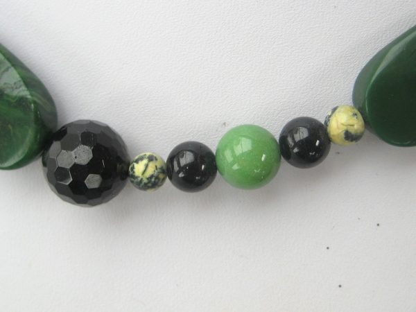 Zoom auf einzelnen helle sowie dunkler grüne und schwarze Steine einer Edelsteinkette aus Jade, Serpentin und Turmalin.