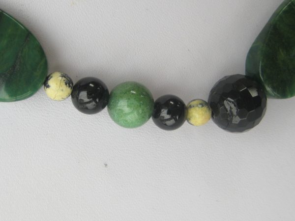 Zoom auf einzelnen helle sowie dunkler grüne und schwarze Steine einer Edelsteinkette aus Jade, Serpentin und Turmalin.