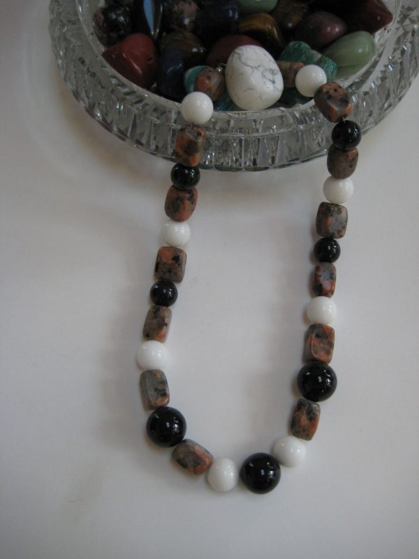 Eine Edelsteinkette aus Turmalin, Jade und Jaspis läuft aus einer Glasschale.