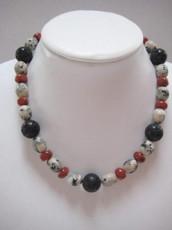 Eine Edelsteinkette aus Jaspis, Lavastein und Granit auf einer weißen Damenbüste. Man sieht ovale Granitsteine in verschiedenen grauen Farbentönen, schwarze Lavakugeln, und Jaspisquader.