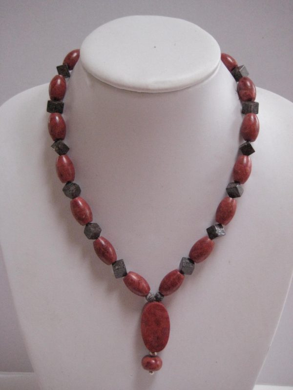 Eine Edelsteinkette aus Koralle und Achat mit einem Anhänger, der eine Perle aus einer Schaumkoralle beinhaltet - auf einer Damenbüste.