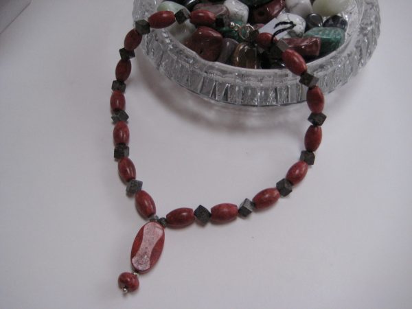 Eine Edelsteinkette aus Koralle und Achat mit einem Anhänger, der eine Perle aus einer Schaumkoralle beinhaltet, fließt aus einer Glasschale.