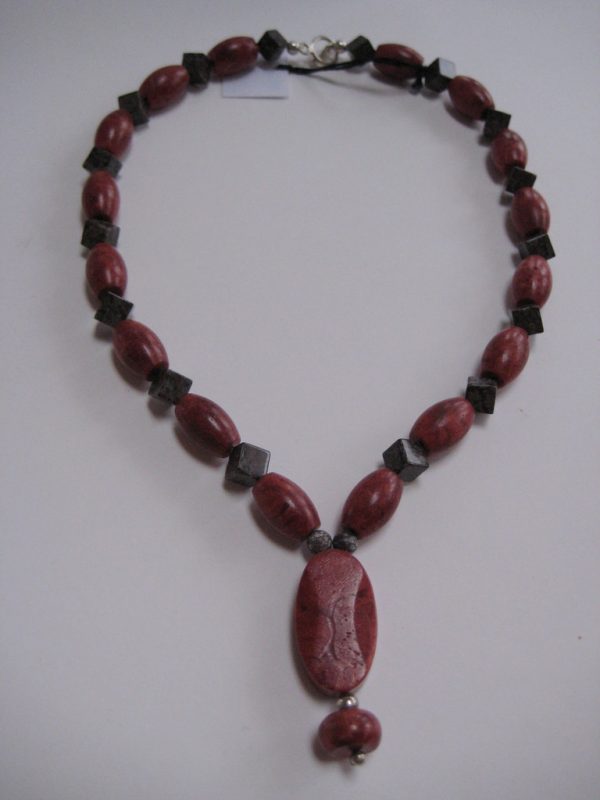 Eine Edelsteinkette aus Koralle und Achat mit einem ovalen Anhänger, der eine Perle aus einer Schaumkoralle beinhaltet.