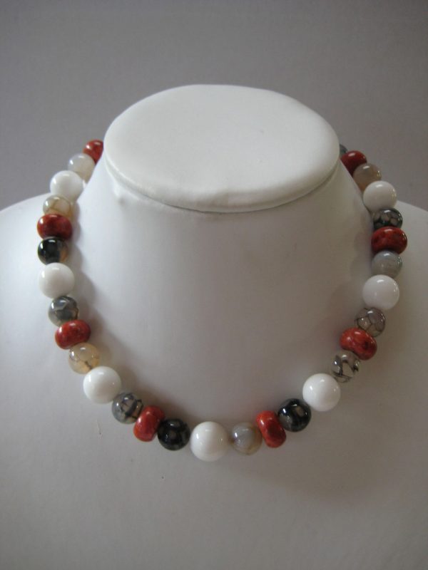 Eine Edelsteinkette aus Koralle, Jade und Achat in Rot-, Weiß-, Grau- und Schwarztönen auf einer weißen Damenbüste.