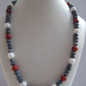 Eine Edelsteinkette aus Koralle und Jade in rot, blau und weiß auf einer weißen Büste.