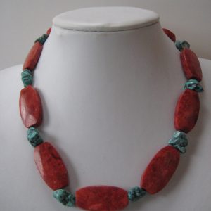 Eine Edelsteinkette aus Koralle und Türkis auf einer weißen Damenbüste. Zu sehen sind rote, ovale Korallen und kleinere Türkisnuggets.