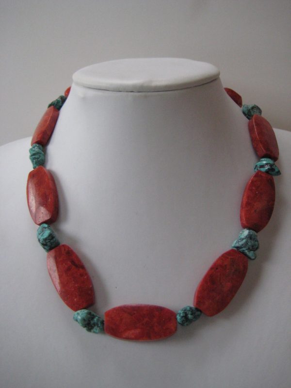 Eine Edelsteinkette aus Koralle und Türkis auf einer weißen Damenbüste. Zu sehen sind rote, ovale Korallen und kleinere Türkisnuggets.