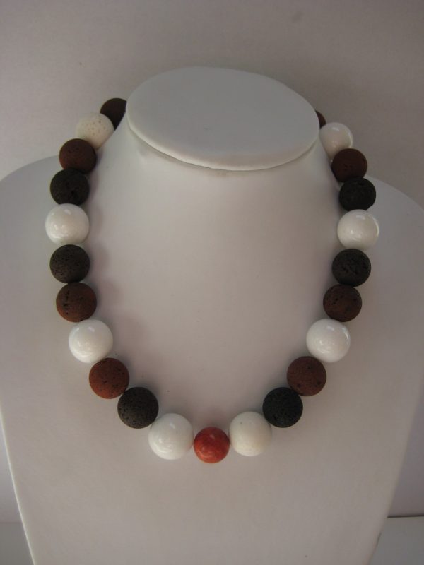 Eine Edelsteinkette aus Lavastein, Jade und Koralle in schwarz, weiß und braun auf einer weißen Damenbüste.
