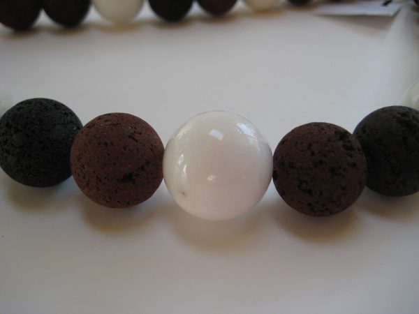Zoom auf die weiße Jadekugel einer Edelsteinkette aus Lavastein, Jade und Koralle in schwarz, weiß und braun.