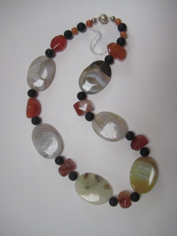 Aufgelegte Edelsteinkette aus Onyx, Achat und Karneol. Sie besteht aus Achat-Elipsen in verschiedenen Farbtönen mit Onyxkugeln und orangen Karneolnuggets.