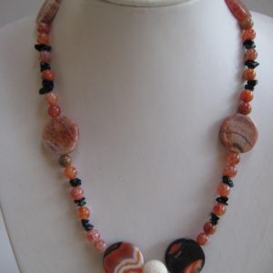 Eine Edelsteinkette aus Onyx, Karneol und Koralle auf einer weißen Damenbüste.
