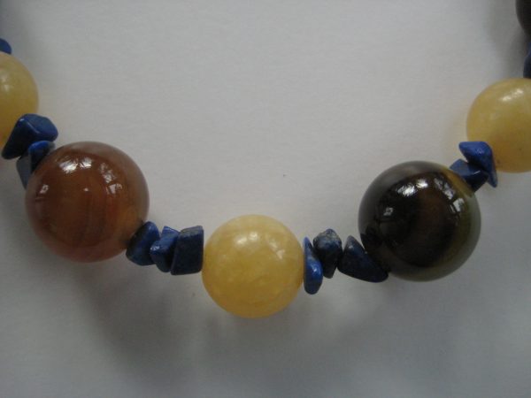 Zoom auf einen gelben und zwei braune Steine einer Edelsteinkette aus Orangencalzit, Lapislazuli und Achat.