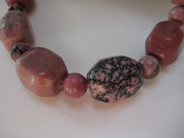 Zoom auf einzelne Steine einer Edelsteinkette aus Rhodonit. Man sieht große rosefarbene Rhodonit Quader und Kugeln.