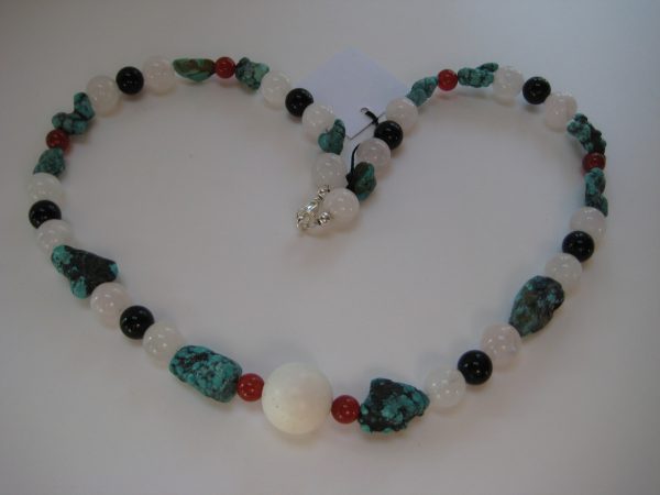 Zu einem Herz gelegte Edelsteinkette aus Türkis, Rosenquarz, Karneol und Onyx auf einer weißen Damenbüste. Die Steine sind türkis, rose, weiß und schwarz.