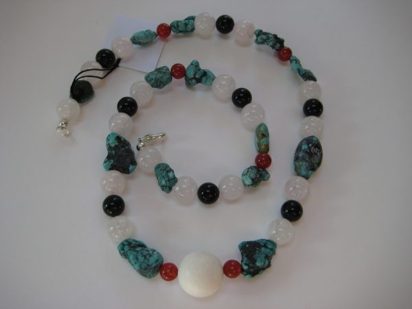 Zu einer Schnecke gelegte Edelsteinkette aus Türkis, Rosenquarz, Karneol und Onyx auf einer weißen Damenbüste. Die Steine sind türkis, rose, weiß und schwarz.