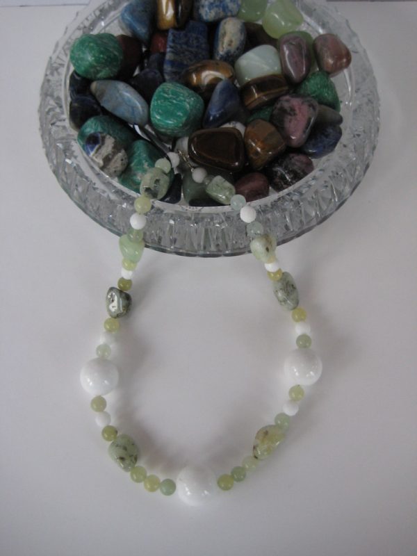 Eine Edelsteinkette aus Jade, Prehnit und Serpentin in frühlingsfrischen grünen Farben fließt aus einer Glasschatulle.